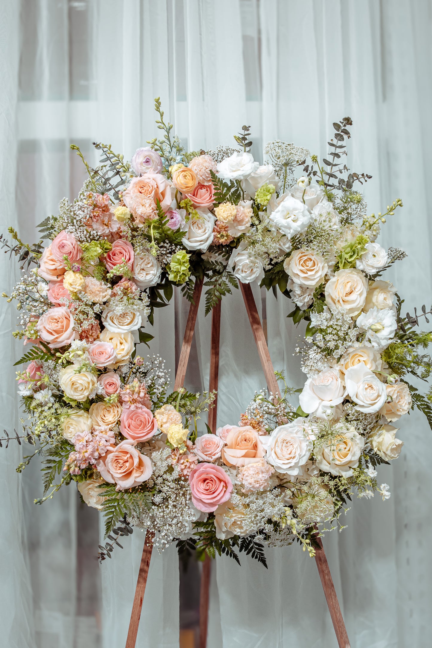 A delicate wreath of pastel blooms arranged in an organic, natural style.A timeless symbol of peace, love,and remembrance.